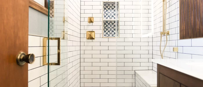 Blue Pattern Tile Shower – Fort Collins Project bathroom remodel featuring crisp white subway tiles with dark grout, custom blue patterned floor tile, and modern gold fixtures. This elegant space includes a glass-enclosed shower, built-in bench, and decorative recessed niche — combining timeless design with functionality, crafted for Colorado living.
